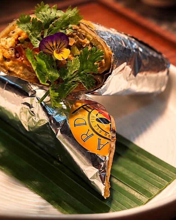 A kathi roll wrapped in foil on a banana leaf