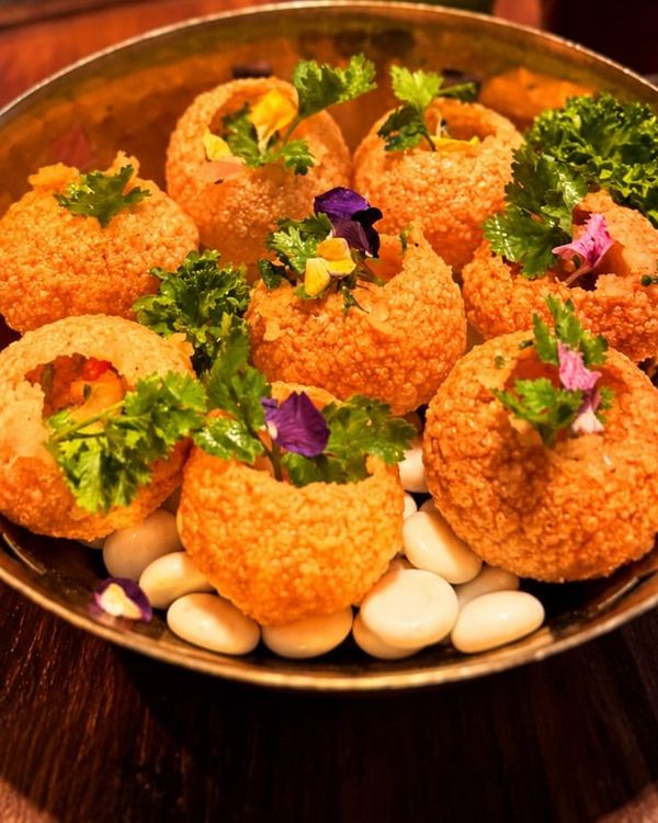 Pani puri in a hammered brass bowl, garnished with edible flowers