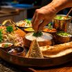 A thali of rice, naan, curries, salad and papad in copper bowls